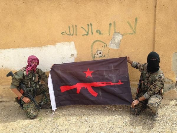 Two people in balaclavas hold a black flag depicting a gun and red star.